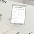 A tablet device on a small stand displaying a lesson overview planner template on a white desk with a notebook, pencil, and plant in a bright indoor setting.