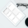 A tablet displaying a black-and-white lesson planner template, arranged on a light surface with eyeglasses and a lined notebook nearby.