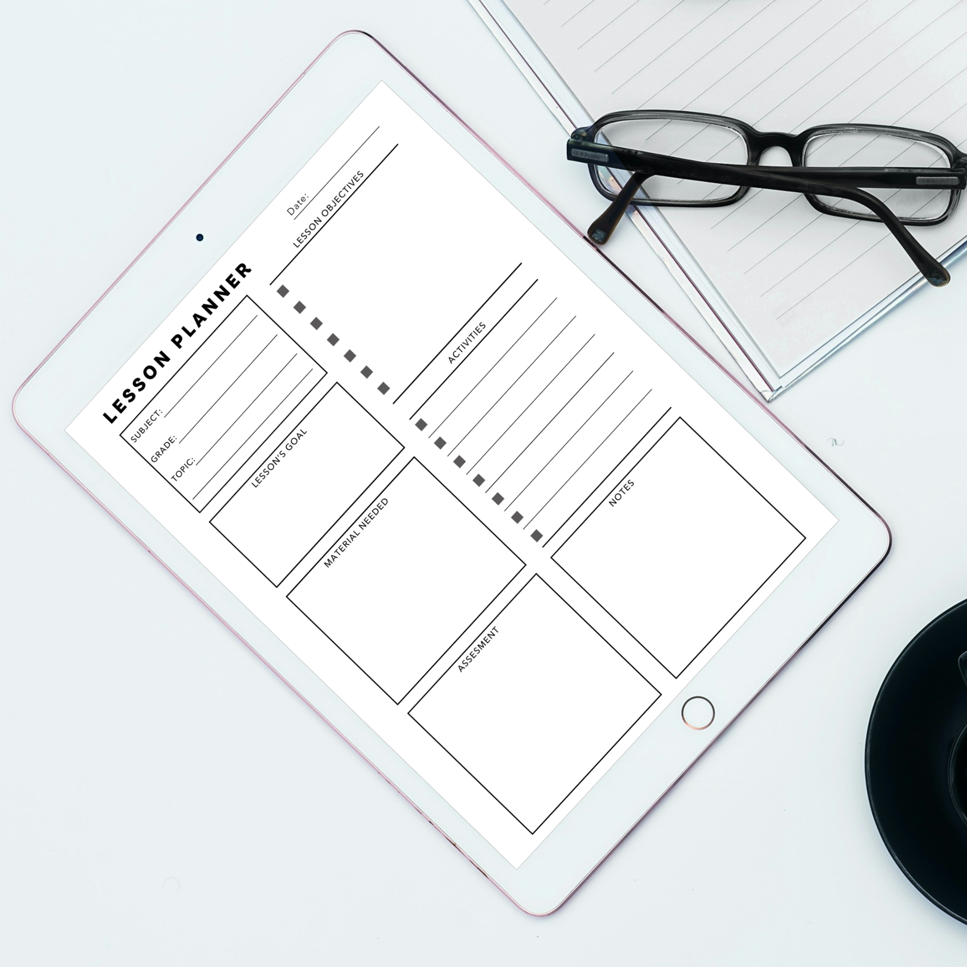 A tablet displaying a black-and-white lesson planner template, arranged on a light surface with eyeglasses and a lined notebook nearby.