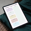 A tablet displaying a Teacher's Daily Planner layout, resting on a dark green fabric surface with a woven brown surface in the background.