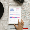 Digital travel budget planner PDF page one shown on iPad featuring a bold purple and pink design with destination field, dates days travelers home currency trip currency and exchange rate fields, budget summary section with planned total actual total contingency difference grand planned and daily per person fields, savings tracker with budget to save per trip saved so far and remaining columns, and variable costs tracker for food and drinks local transport activities shelter and accommodation shopping.